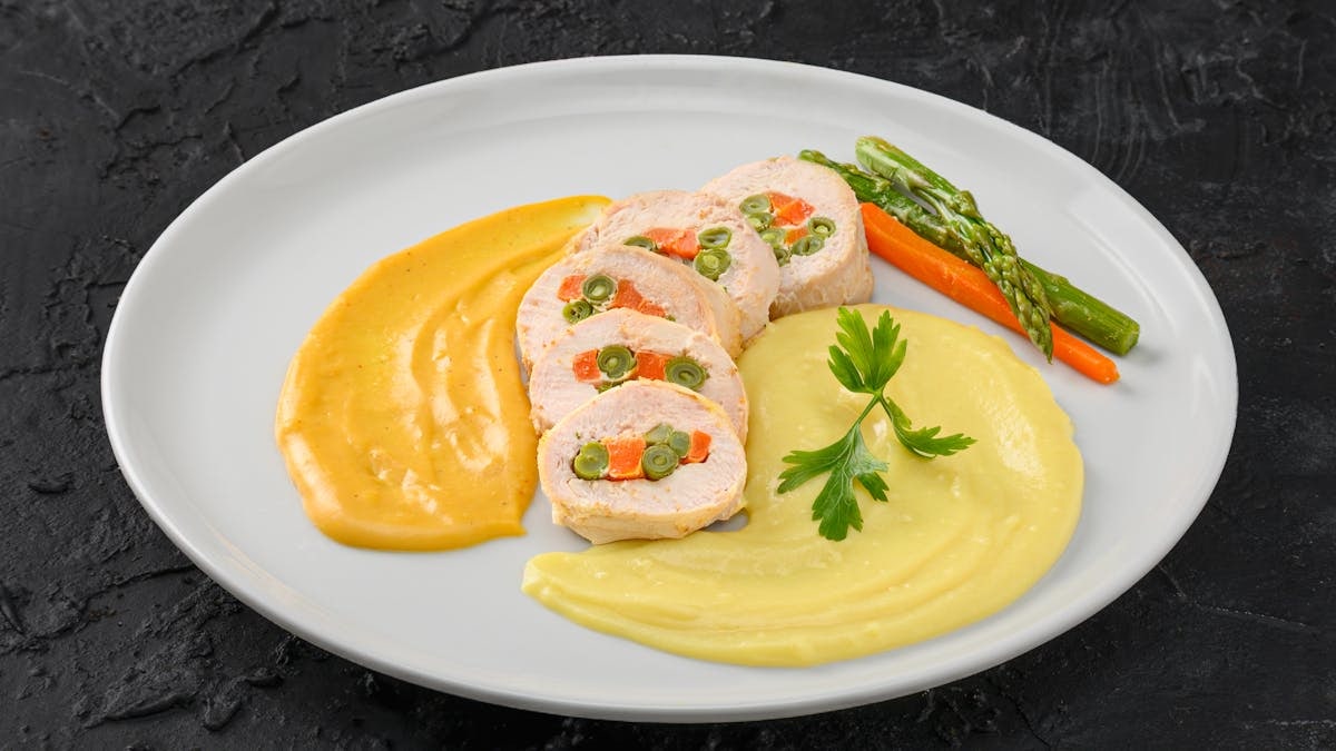 Elegant stuffed chicken breast with mixed vegetables and puree, artfully plated for a gourmet experience.